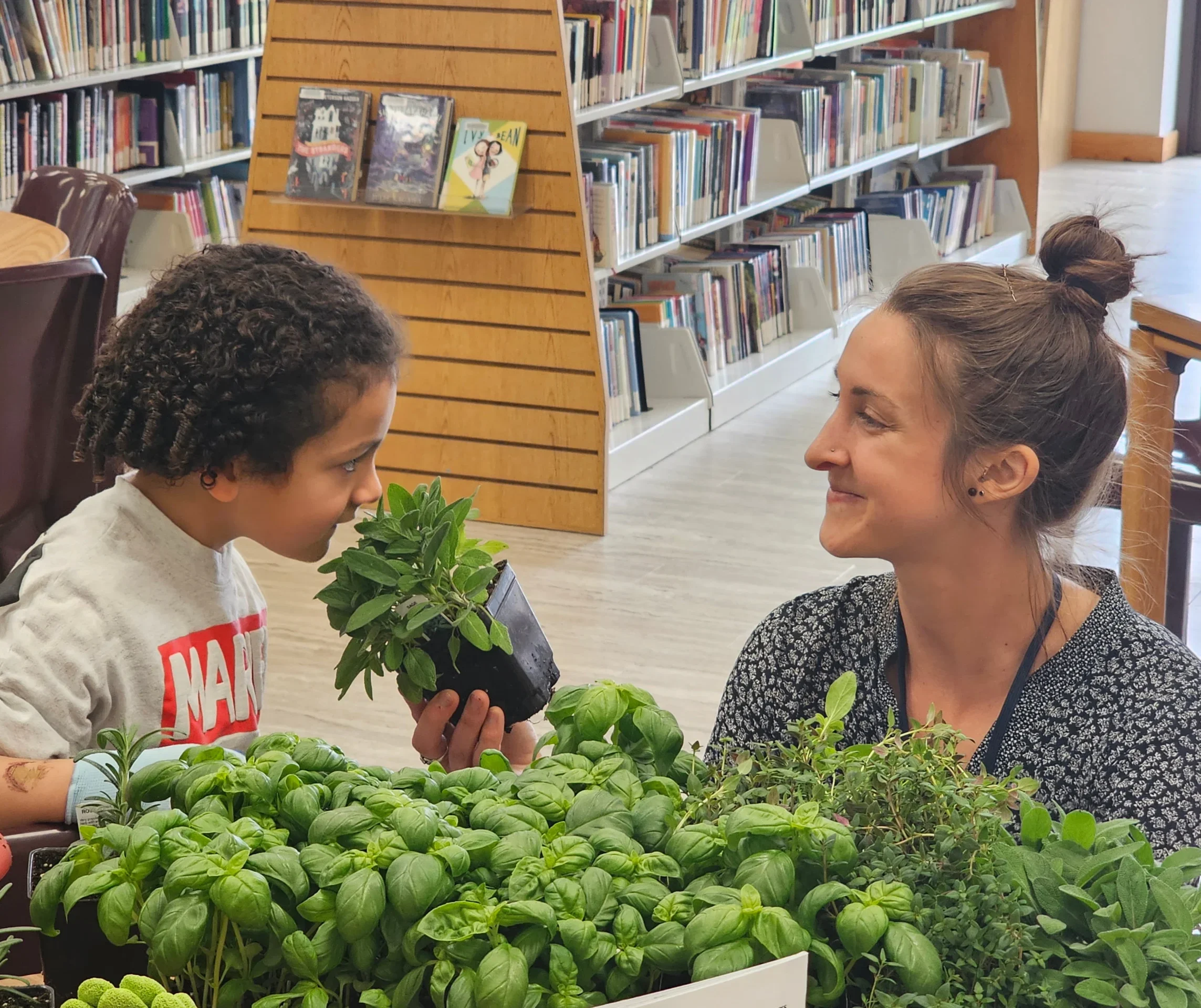 woman holds a potted herb to a child's nose so they can smell it